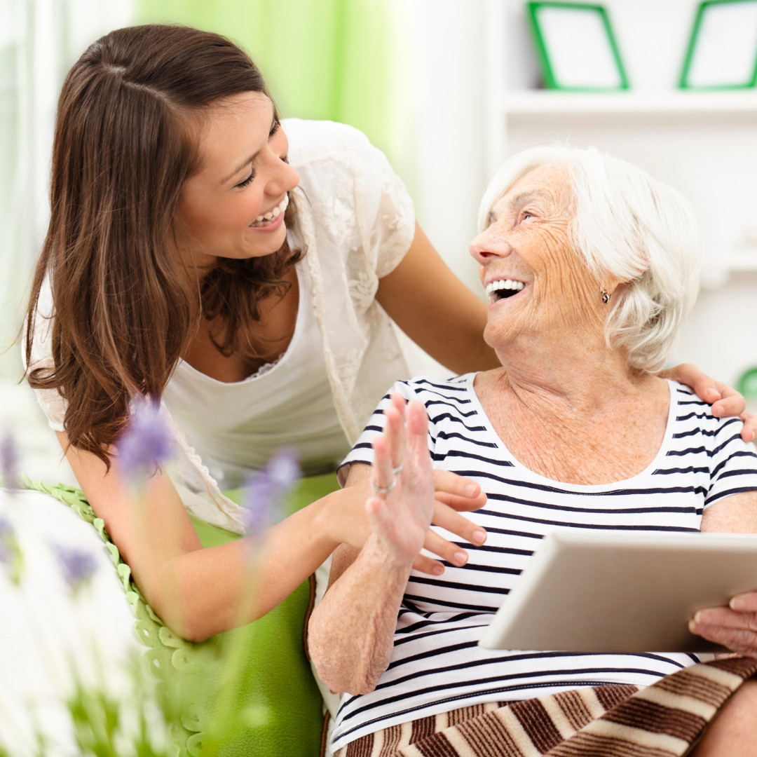 Elderly lady looking up at younger woman while laughing and holding a notepad
